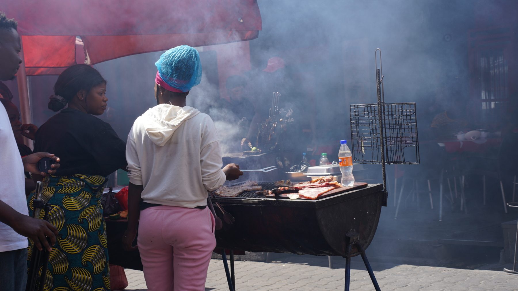 Smoke rising from open drum grills at a Lusaka food market